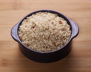 Integral, brown rice pile in porcelain dish isolated on wooden table