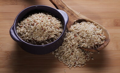 Integral, brown rice in porcelain dish and spoon pile isolated on wooden table