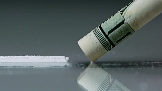 Drug Abuse. A rolled banknote snorting a line of cocaine powder. Problems with drugs concept. Grey background. Close-up macro shot.