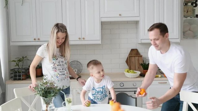 a young father shows the son in the kitchen how to juggle oranges