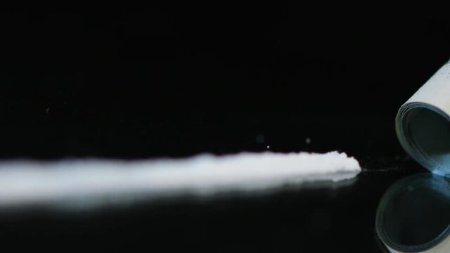 Drug Abuse. A rolled banknote snorting a line of cocaine powder. Problems with drugs concept. Black background. Close-up macro shot. Soft focus