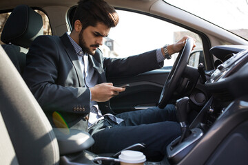 Handsome businessman texting message on the phone while driving  car unsecured without fastening seat belt.Safety concept.