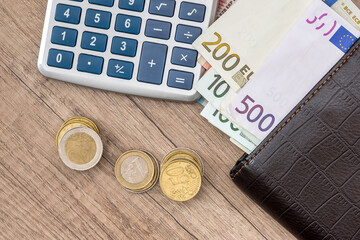 euro in purse with calculator and coin on desk.
