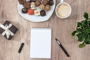 empty notepad with pen, chocolate, and cup of cappuccino.