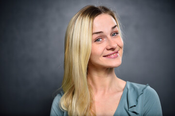Blonde girl with a cunning smile on a gray wall background