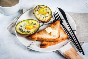 Healthy vegan breakfast. Diet. Baked avocado with egg and fresh salad from arugula, toast and butter. On a white marble plate, a light concrete table. A cup of coffee. Copy space