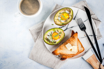 Healthy vegan breakfast. Diet. Baked avocado with egg and fresh salad from arugula, toast and butter. On a white marble plate, a light concrete table. A cup of coffee. Copy space