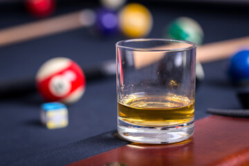 Glass of whiskey on billiard table with cue and billiard balls in background.