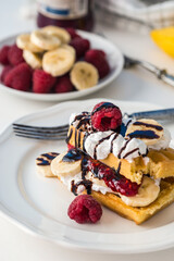 Belgian waffles with raspberries and bananas on white plate and white background.