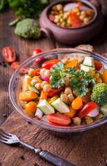 Vegetable salad in glass bowl with broccoli and tomatoes on dark wooden table.