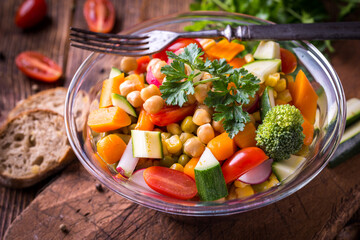 Vegetable salad in glass bowl with broccoli and tomatoes on dark wooden table.