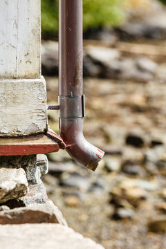 Thin drainpipe on cottage wall, rocks background