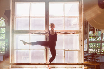 Male ballet dancer is dancing in front of a large window, standing on the windowsill.