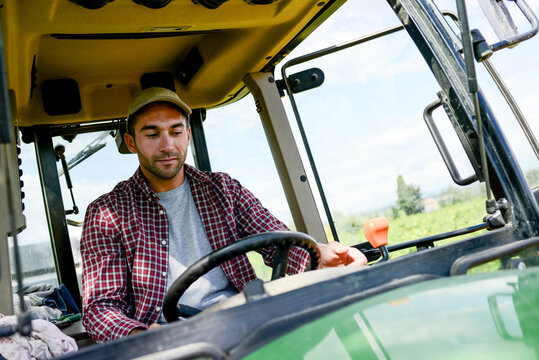 handsome young male farmer driving his tractor during harvest in the field countryside