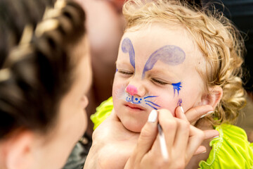 woman painting face of kid outdoors