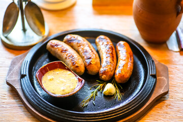 Sausages are grilled on a black frying pan with mustard.