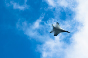 A military fighter high in the sky, piercing clouds of vapor breaks.