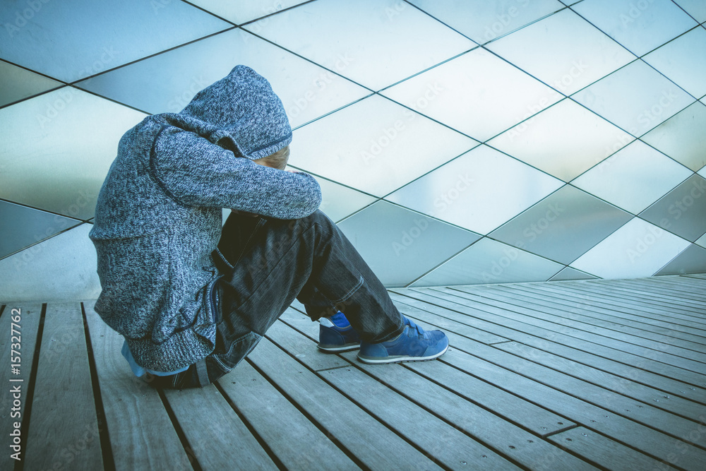 Wall mural Sad, lonely, unhappy, disappointed child sitting alone on the ground outdoors