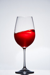 Fragile elegant wineglass of red wine standing against light background.