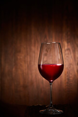Half-full fragile wineglass of red wine standing on a wooden background.