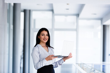 Successful woman staning in office holding laptop in her hands