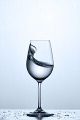 Wave of the drinking water in the wineglass while standing on the glass with water bubbles against light background.