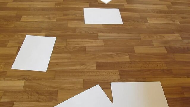 White clean sheets of office paper fall on the wooden floor - 12sec. Indoor video for offices or education, soundless