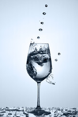 Fresh transparent water pouring with water bubbles in a glass standing on the glass against light background.