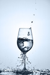 Drinking pure water poured into a transparent wineglass standing on the glass with droplets against light background.