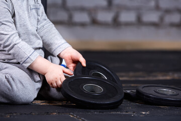Close-up view photo of little sporty child with barbbell against brick wall at the cross fit gym.