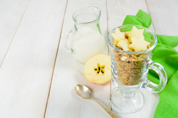 Health breakfast with milk, granola, fresh apple and kiwi on white wooden table