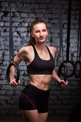 Fototapeta na wymiar Image of beautiful young sporty woman in the black sportwear doing pull-ups exercise using gymnastic rings.