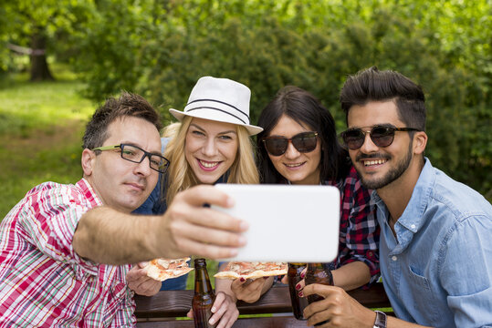 Group of young people  in the park eating pizza, drinking beer and taking selfie