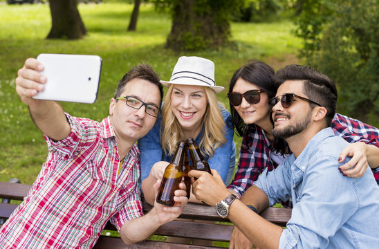 Group of friends having fun in the park while toasting beer and taking selfie