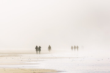 people walking with sandstorm on beach