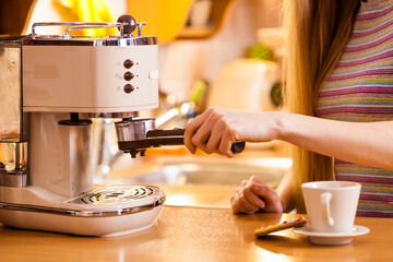 Woman in kitchen making coffee from machine