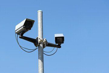 Two cctv surveillance cameras on a high street pylon against the clear blue sky, concept for safety and security against vandalism, crime or terrorism
