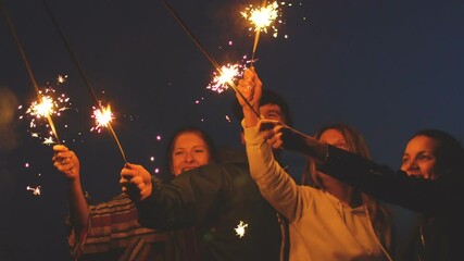 Slowmotion Group of young friends having a beach party. Friends dancing and celebrating with sparklers in twilight sunset - Powered by Adobe
