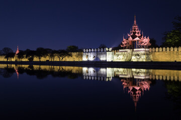 Fototapeta na wymiar Lit citadel's wall, bastion and pyatthat (spire) and moat at the royal Mandalay Palace in Mandalay, Myanmar (Burma) at night.