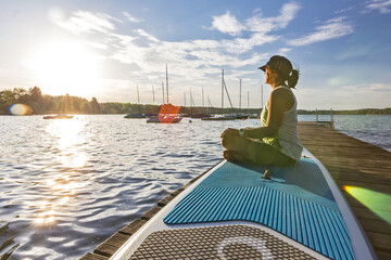 Frau geniesst die Abendsonne auf einem Surfbrett am Steg
