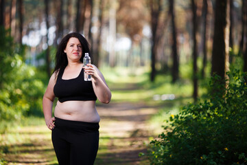 Young overweight smiling woman with a bottle of clear water outdoors