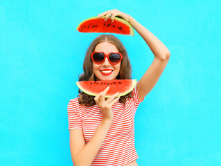 Pretty happy smiling woman is having fun with slices of watermelon over colorful blue background