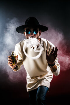 Handsome stylish man in hat and sunglasses making rings with vapor.
