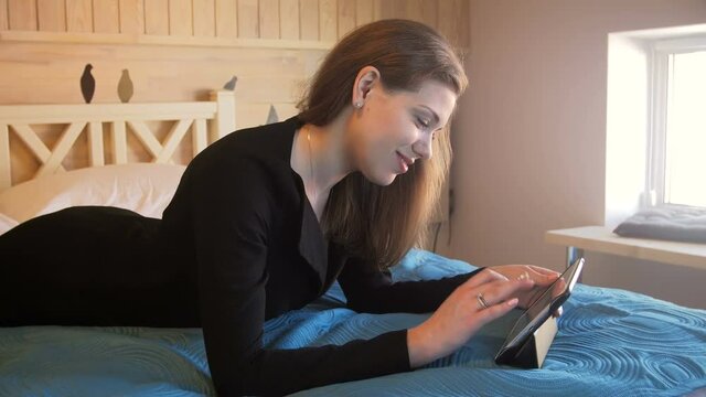 4K footage of beautiful smiling businesswoman lying on bed at hotel room and using digital tablet
