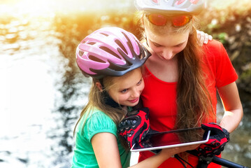 Fototapeta premium Bikes cycling girl. Children rides bicycle. Bicyclist girl watch on tablet computer. Kids looking for way. Dependence of adolescents on gadgets. Sports orienteering.