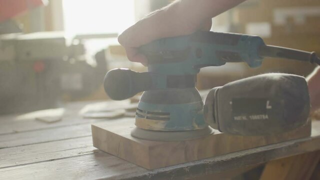 Hands of woodworker carpenter grinding wooden plank in backlight using machine