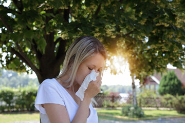Fototapeta premium Pollen allergy. Woman sneezing in a tissue outdoors