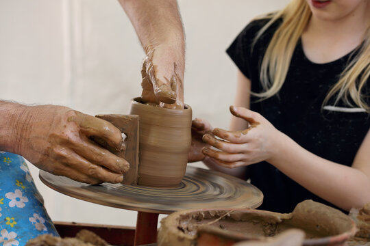 Child in clay studio working on a bowl. Potter sculpting clay pot on a turning pottery wheel