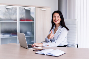 Beautiful woman in office showing thumbs up while working on her laptop