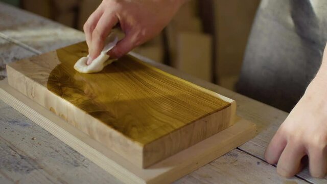 Close up hands of carpenter woodworker rubs lacquer on a wooden plank